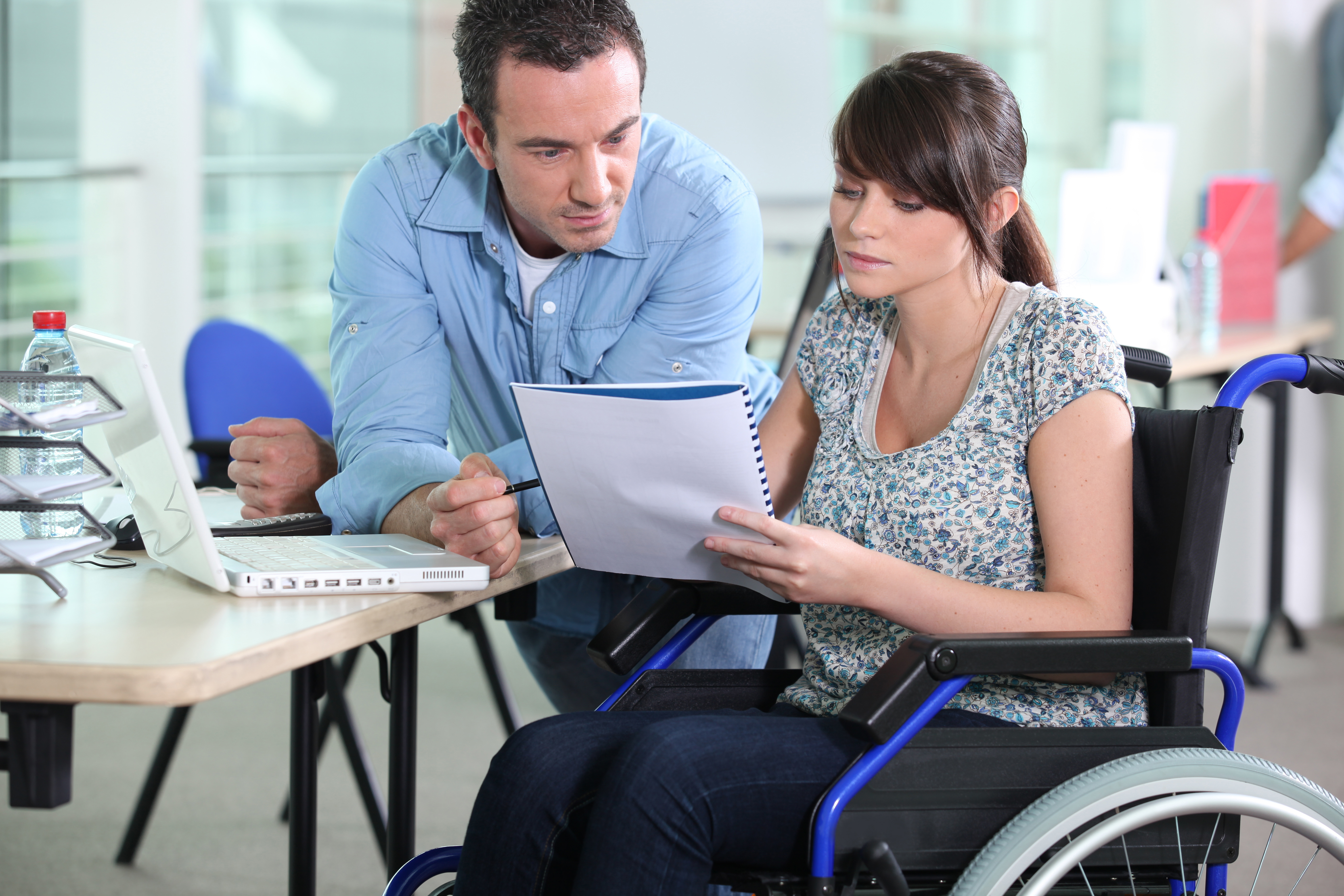 Young professional in wheelchair reading a notebook with a seated colleague