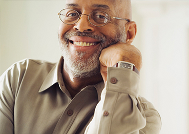 An older African American professor smiles, with his chin resting on his hand
