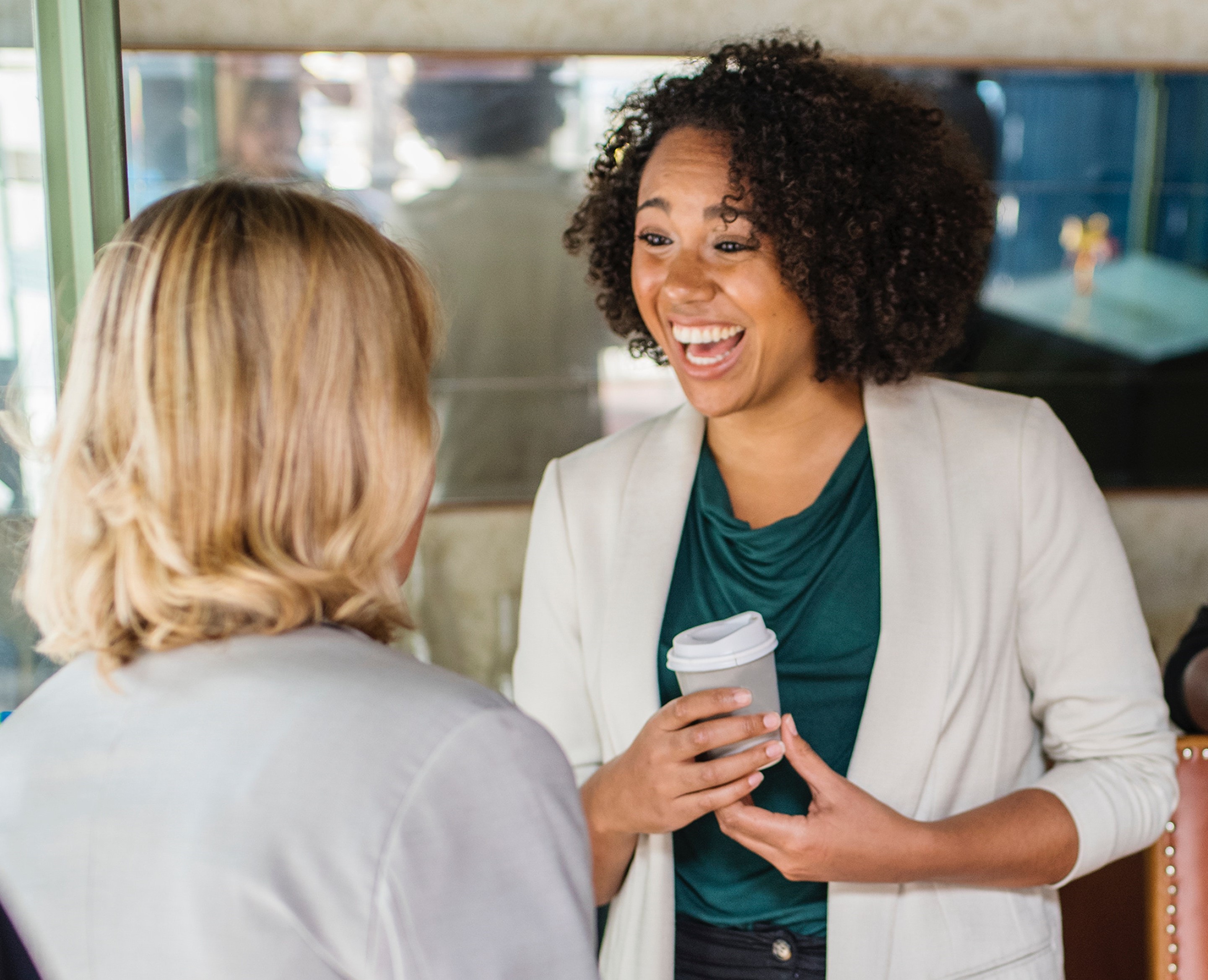 Two colleagues having a conversation. One is holding a cup of coffee.