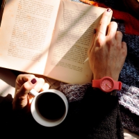 A person holding a coffee cup with a book in her lap