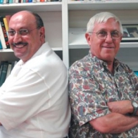 Edward Kaufman and Manuel Hassassian stand back-to-back, smiling, in front of a bookshelf