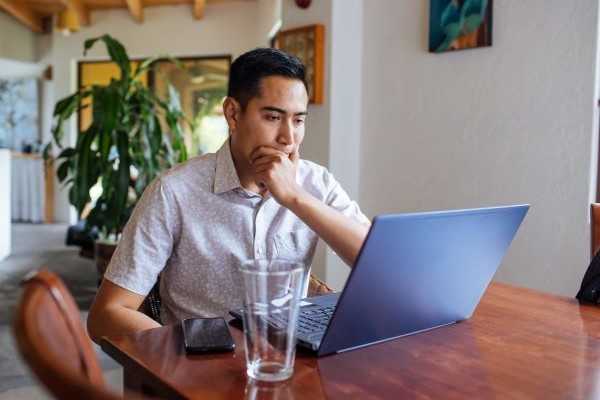 Higher ed job seeker looking at laptop screen, thinking about how explain a career gap to a potential employer