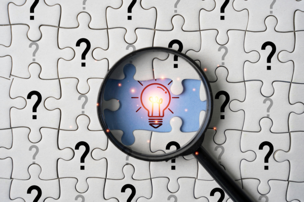 puzzle pieces with question marks on them and magnifying glass in middle with a view of a lightbulb